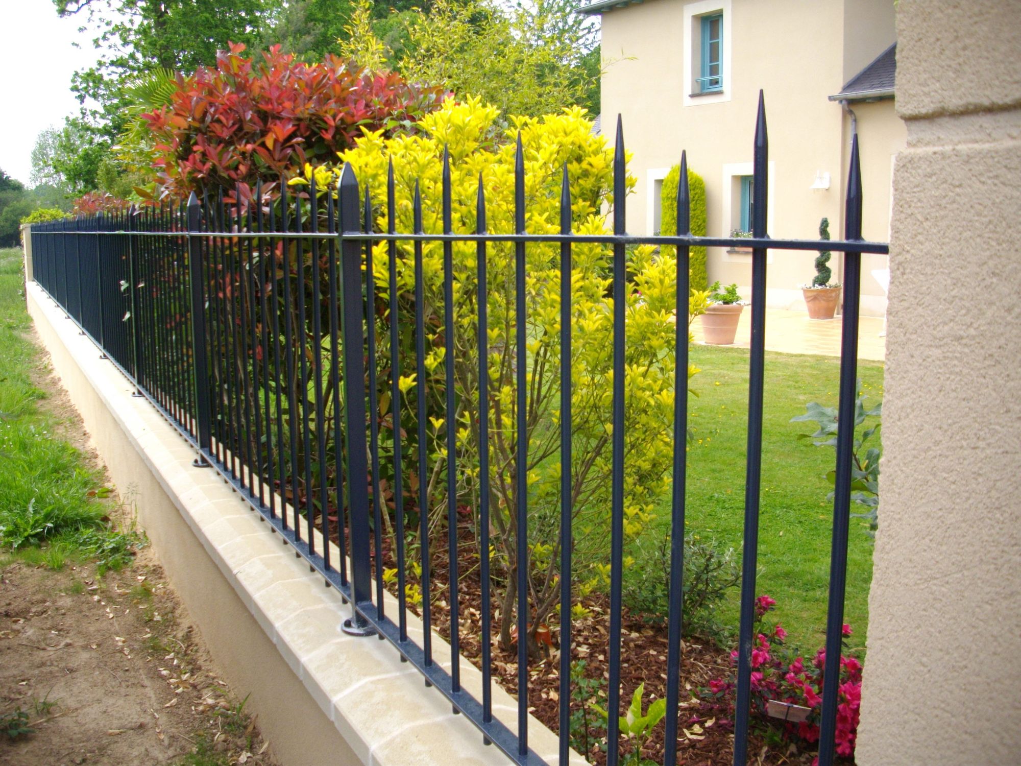 Clôture en acier à barreaudage noir sur muret dans un jardin fleuri