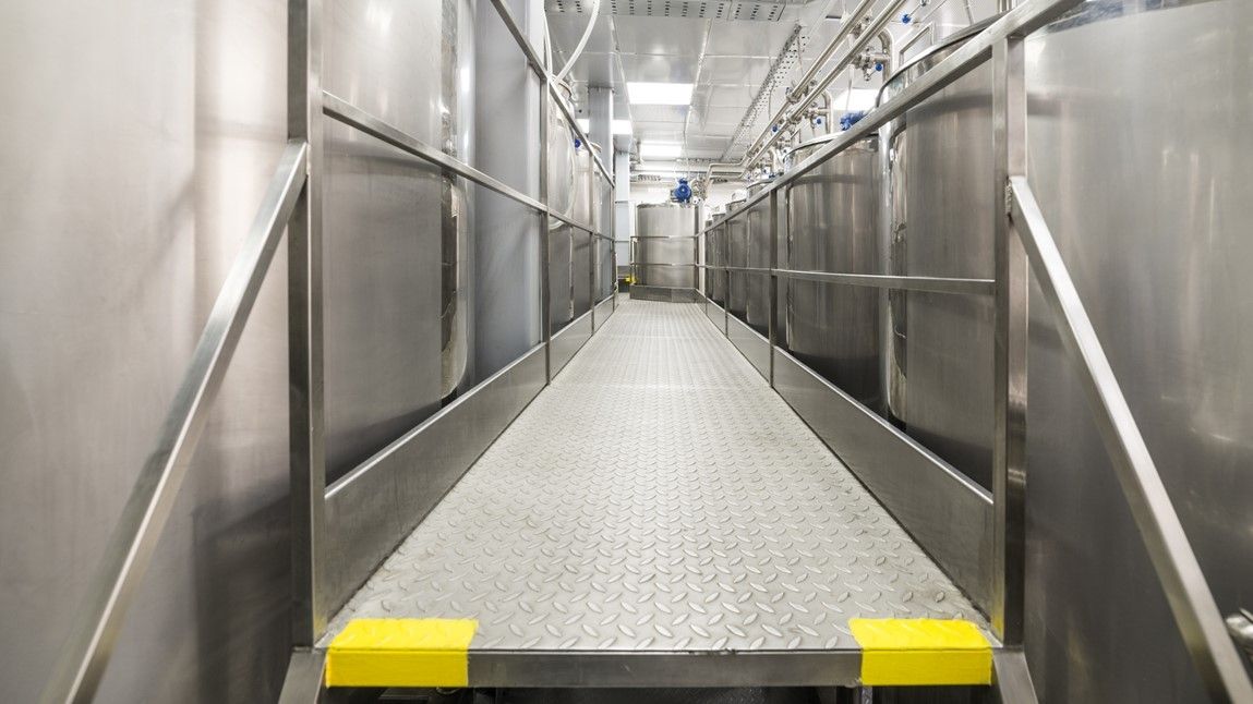 Passerelle en acier avec plancher caillebotis et garde-corps entre deux zones d'un bâtiment industriel